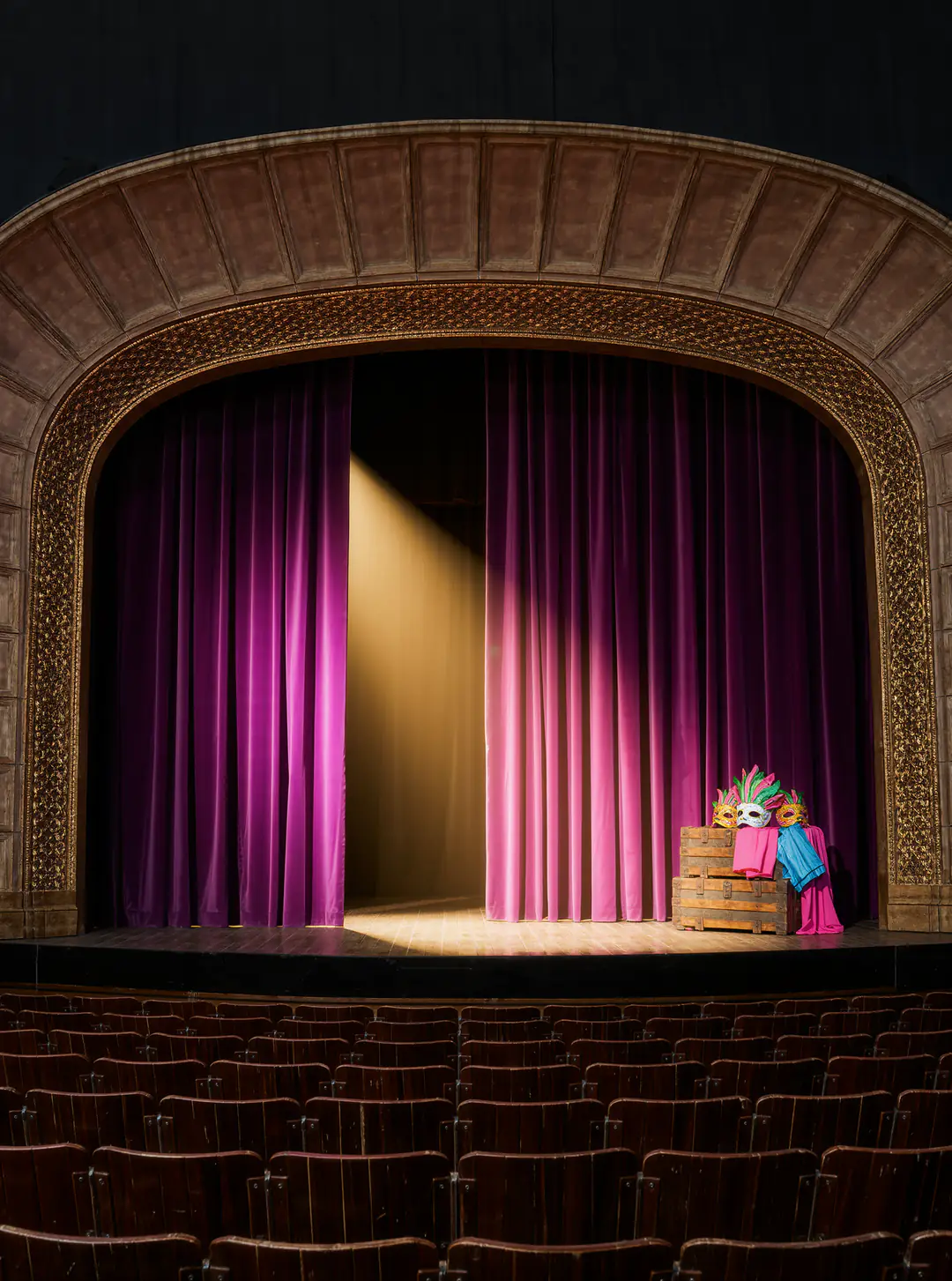 Taller de teatro: un escenario con telón violeta, luces cálidas y máscaras sobre un baúl.